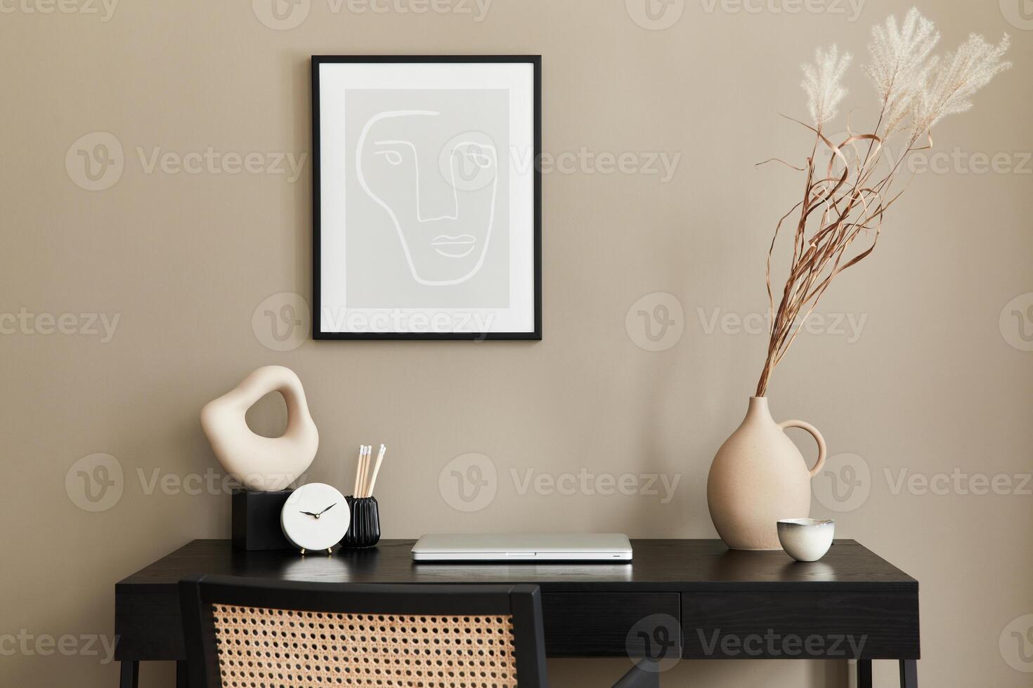 Stylish composition of home office interior with black wooden desk, chair, dried flower in vase, laptop, mock up poster frame, clock and elegant office accessories. photo