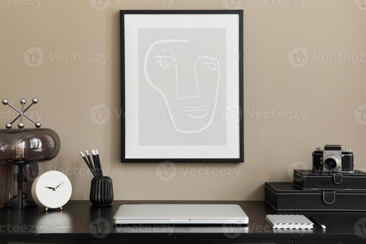Stylish composition of home office interior with black wooden desk, laptop, mock up poster frame, table lamp, photo camera, organizer, clock and elegant office accessories.
