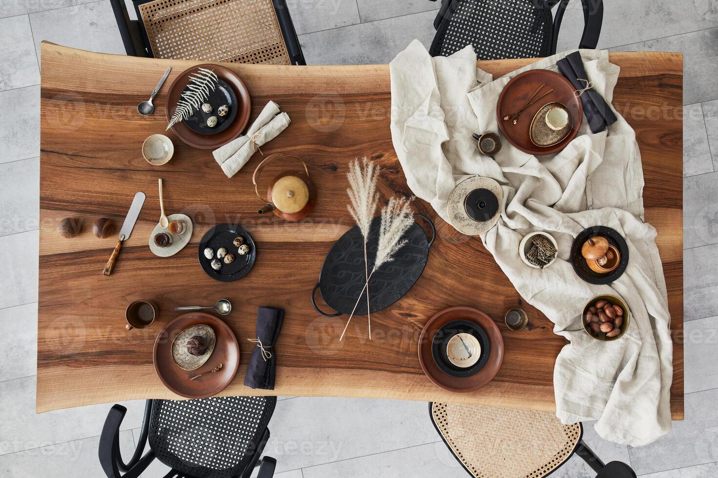 Stylish interior design of dining room with wooden walnut table, chairs, tableware, plates, tablecloth, food, decoration and elegant accessories. Cement floor. Template. Top view. photo