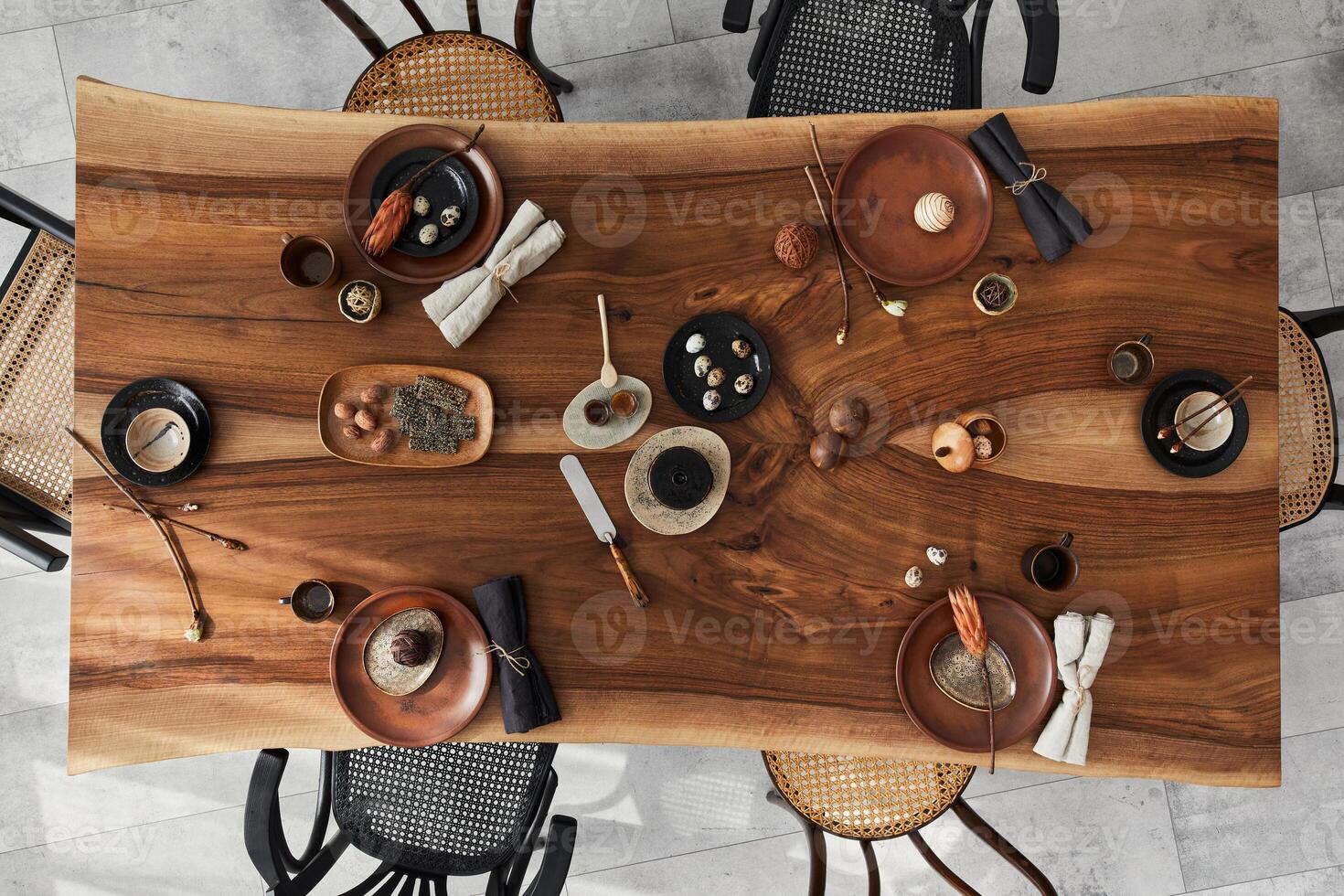 Stylish interior design of dining room with wooden walnut table, retro chairs, tableware, plates, tablecloth, food, decoration and elegant accessories. Cement floor. Template. Top view. photo