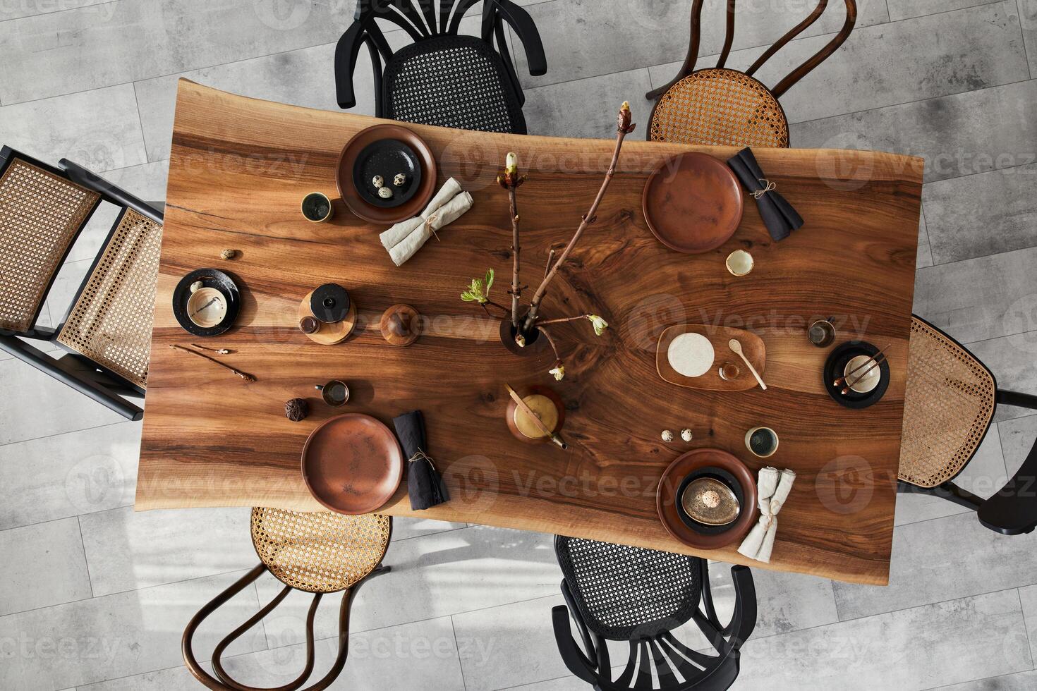 Stylish interior design of dining room with wooden walnut table, retro chairs, tableware, plates, tablecloth, teapot, food, decoration and accessories. Cement floor. Template. Top view. photo
