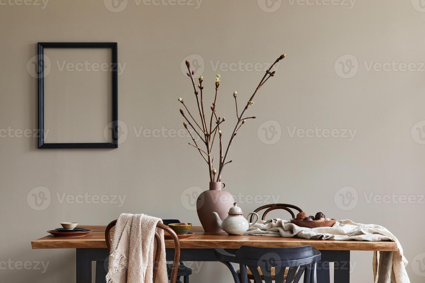 Stylish rustic interior of dining room with walnut wooden table, retro chairs, decoration, dried flower and mock up picture frame in minimalist home decor. photo