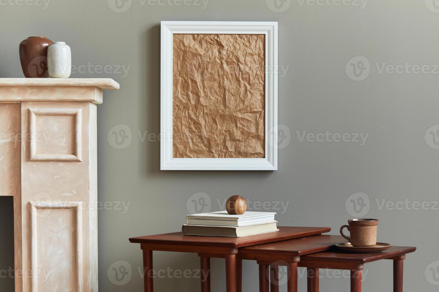 Stylish and luxury interior with white mock up poster frame, rustic chimney, book, wooden stools, mug and elegant accessories in home decor. Template. photo