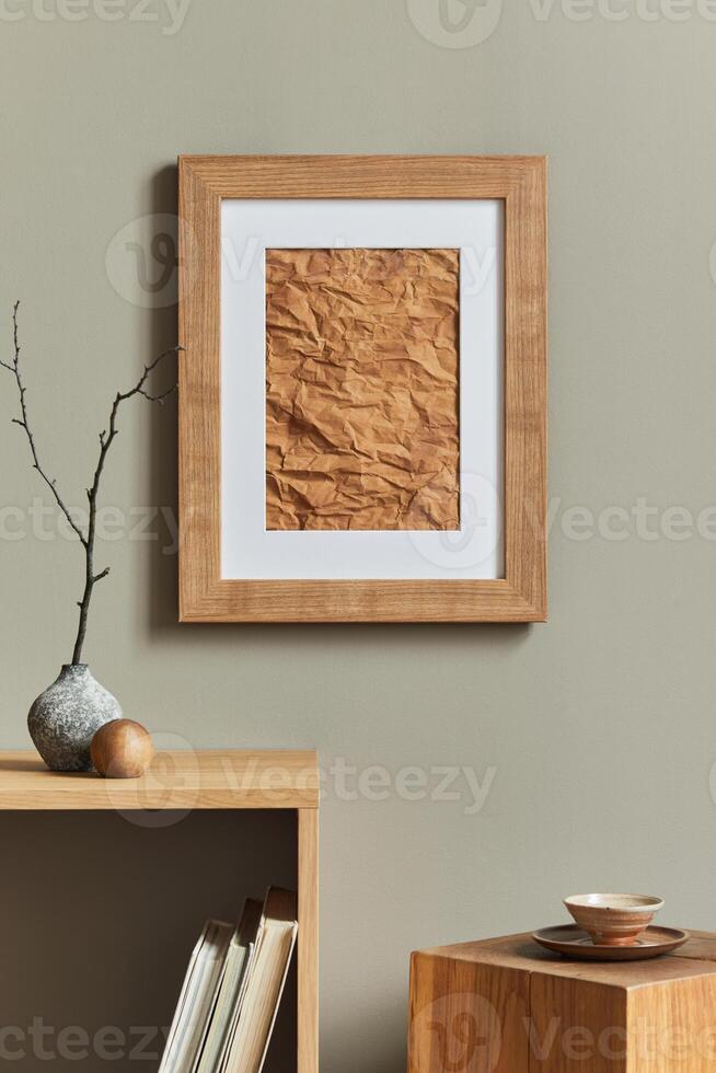 Minimalist composition on wooden shelf with brown mock up poster frame, dried flower in vase, cube, book, cup of coffee and elegant personal accessories in home decor. Template. photo