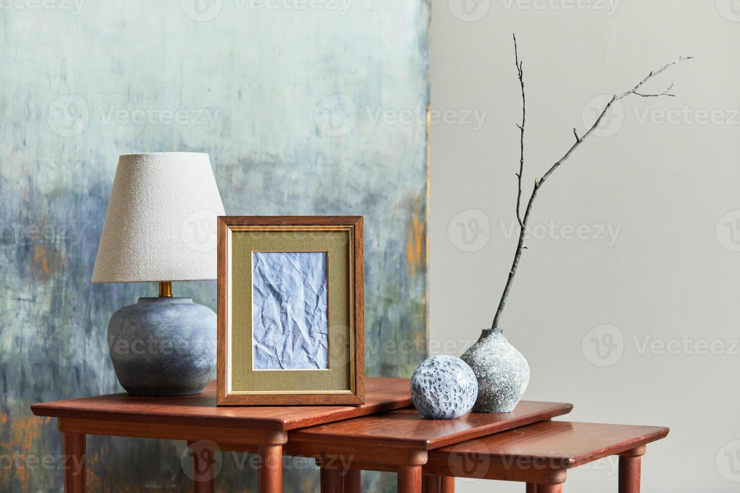 Stylish and luxury interior with brown poster frame, vases, books, wooden stools, mug and elegant accessories in home decor. Template. photo