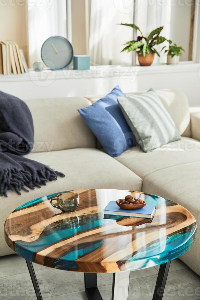 Stylish composition with design epoxy coffee table, sofa, blanket, pillows, decoration and personal accessories in modern home decor. Details. photo