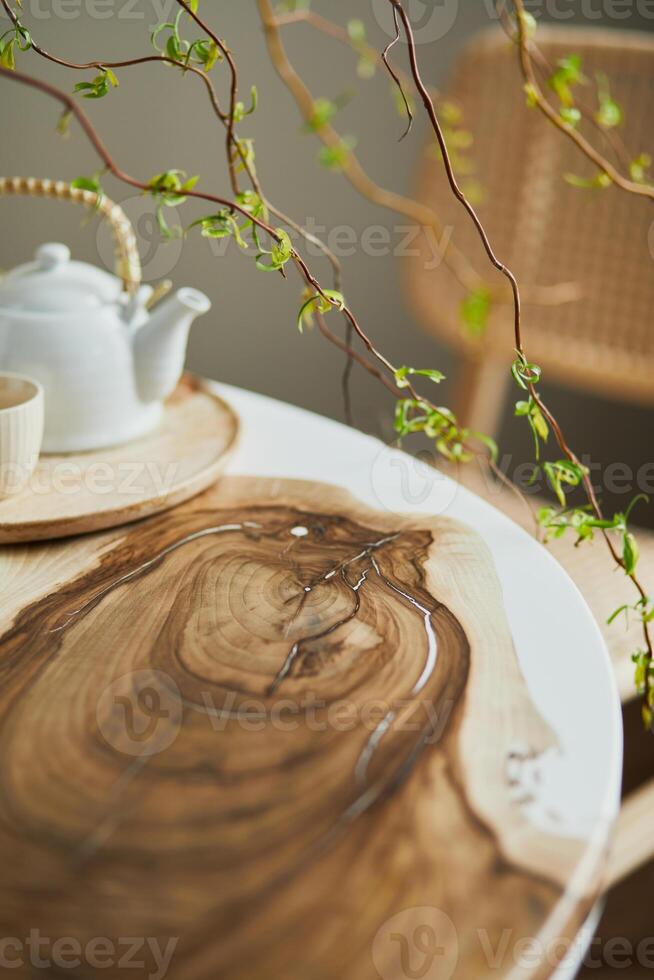 Interior design of stylish dining room interior with family wooden and epoxy table, rattan chairs, flowers in vase and teapot with cups. Template. photo