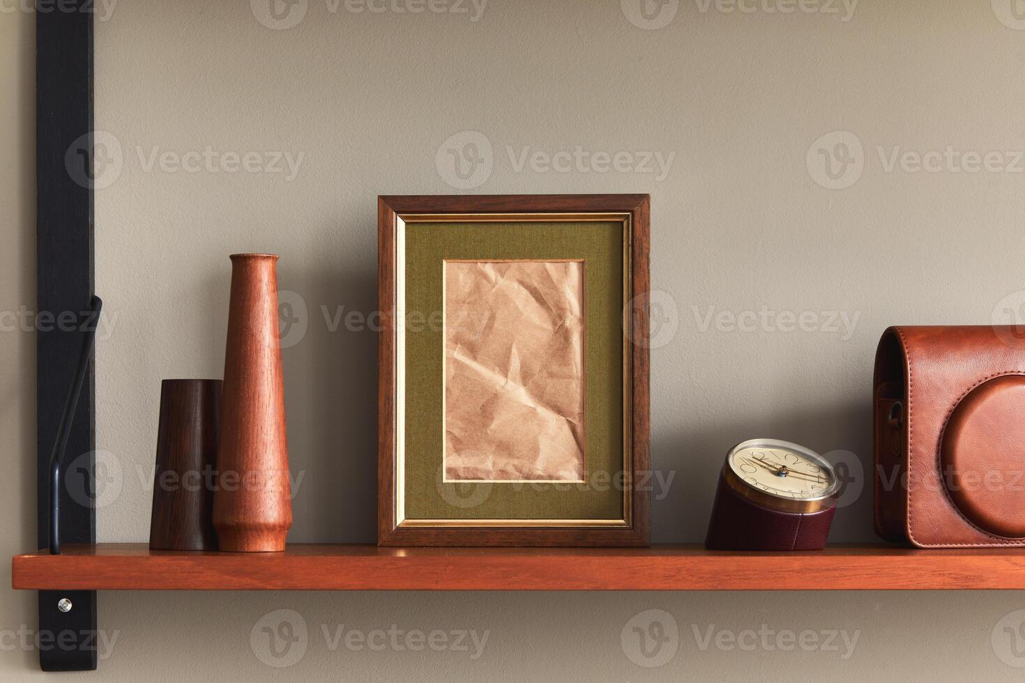 Minimalist composition on wooden shelf with brown mock up picture frame, clock, vase, camera case and elegant personal accessories in stylish home decor photo