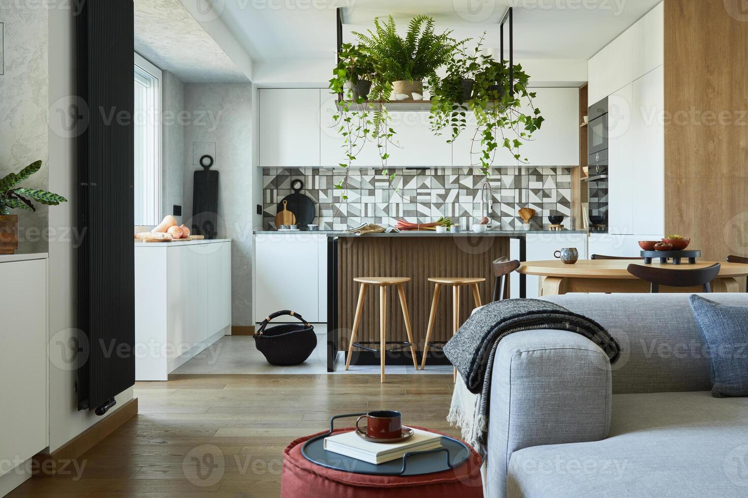 Stylish living room interior design with sofa, pouf and personal accessories. Dining space and kitchen on the background. Creative walls with wooden pannels. Minimalistic style and plant love concept. photo