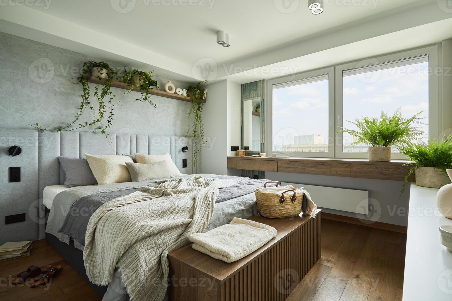 Stylish bedroom interior in modern apartment with small bed, wooden chest, home garden, white bedding, pillows and blanket. Sunny space with grey walls and brown wooden parquet. photo