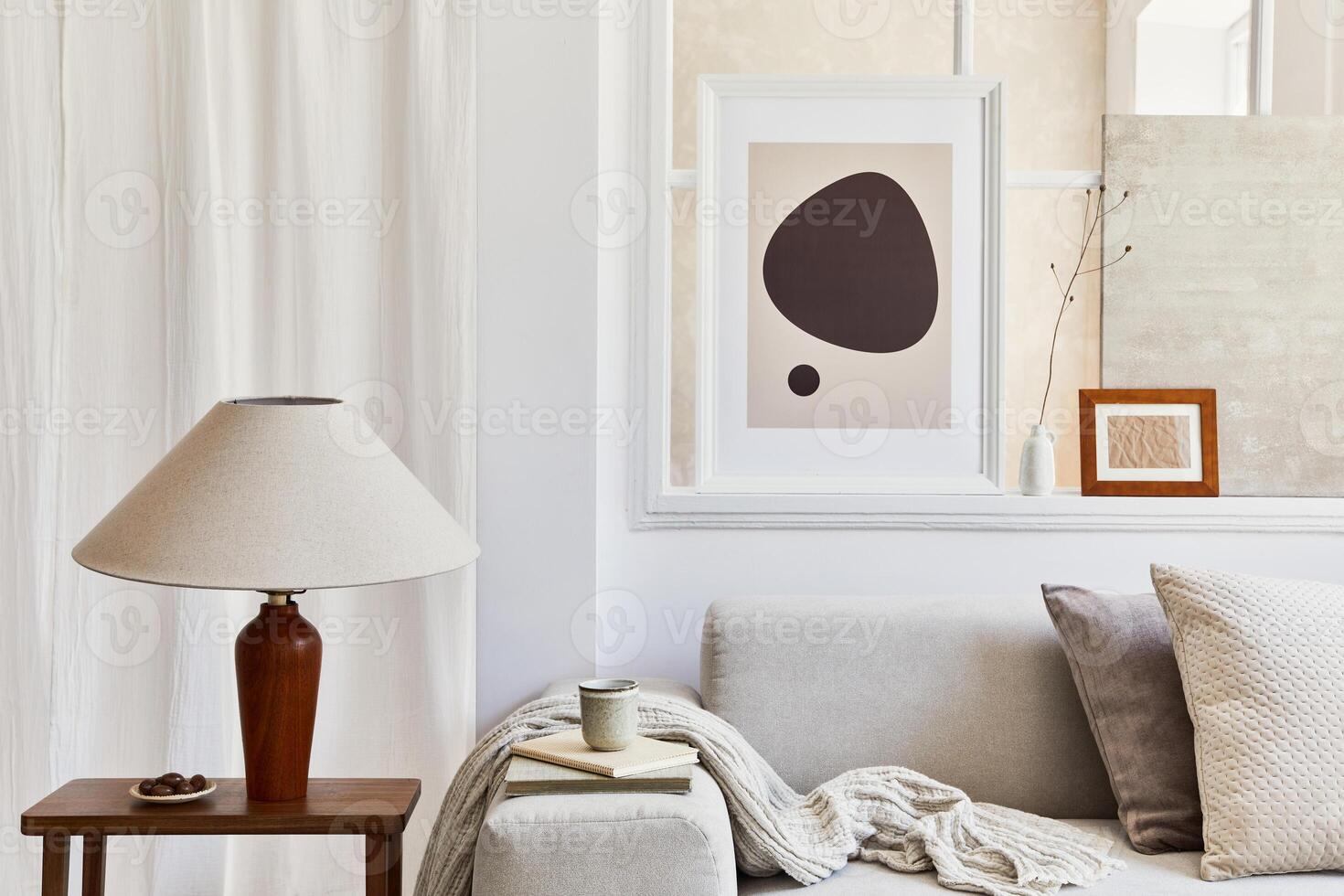 Creative composition of stylish and cozy living room with mock up poster frames, grey sofa, lamp, window, plaid and personal accessories. Beige neutral colors. Template. photo