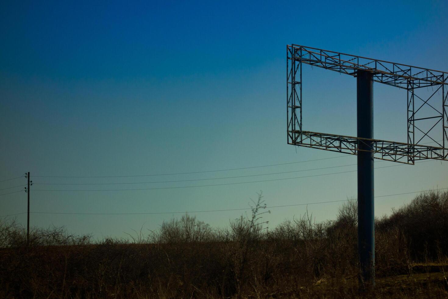 An empty billboard structure stands alone against a clear blue sky in a rural landscape. photo