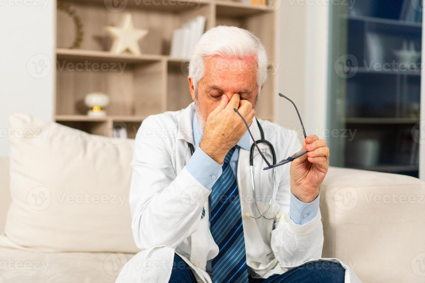 Sad tired mature senior male doctor in medical uniform in hospital or doctor office. Unhappy General Practitioner GP therapist professional healthcare expert in clinic. Healthcare concept photo