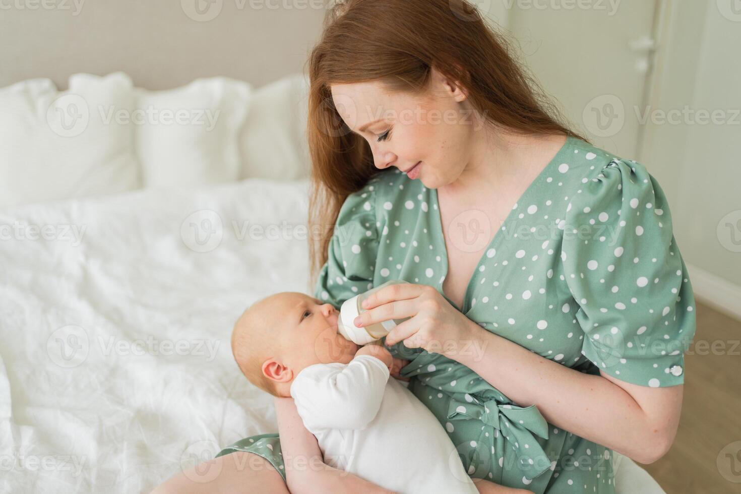 Happy family at home. Mother holding little baby toddler child feeding milk from bottle. Newborn Infant baby girl sucking eating drinking milk. Mom of breast feeding baby. Motherhood happy child photo