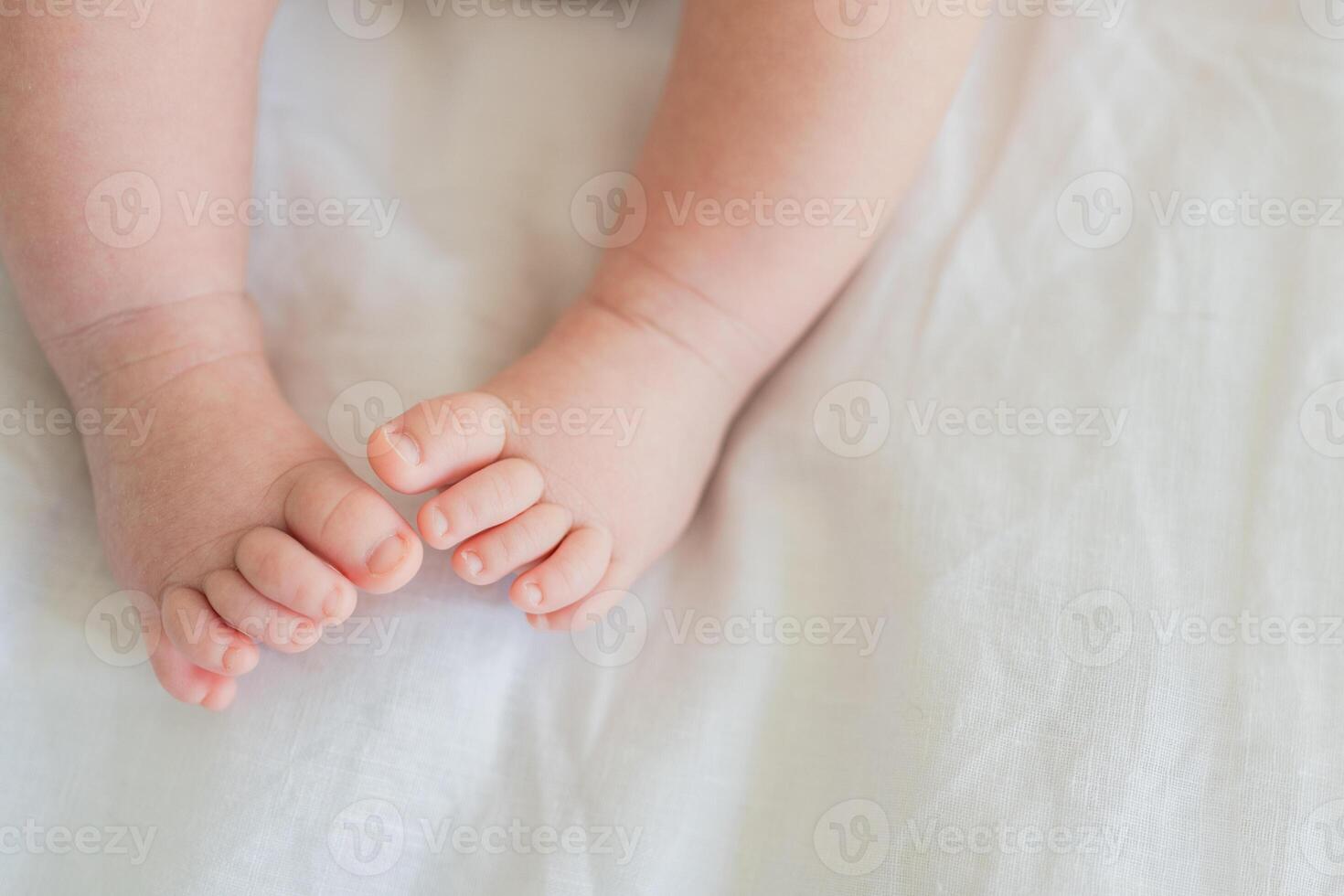 Tiny newborn infant baby feet and toes on white background. Soft newborn baby foot legs under the white blanket. Close up of infant barefeet. Maternity tenderness parenthood birthday. Happy Family photo