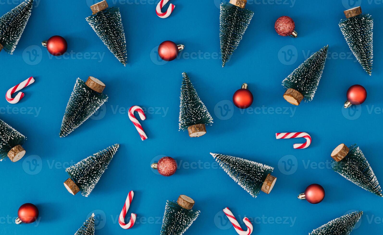 Trendy Christmas pattern made with green Christmas trees, candy canes and red Xmas baubles on blue background. Minimal creative Christmas and New Year concept. Festive holiday backdrop. Flat lay. photo
