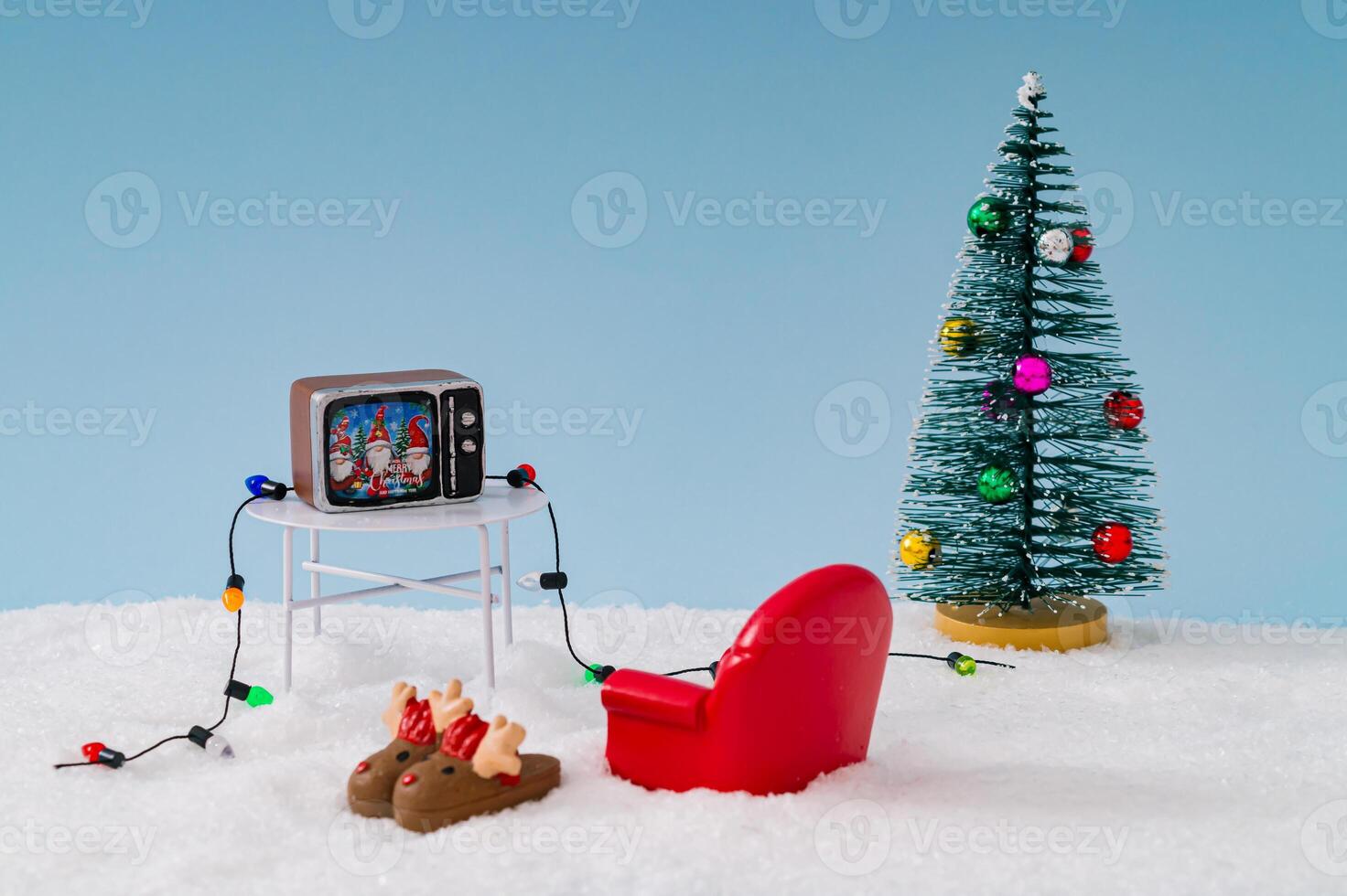 Christmas composition made with Christmas tree, red armchair, Xmas slippers, tv, lights and snow on blue background. Surreal concept for Christmas and New Year movies on television in winter time. photo