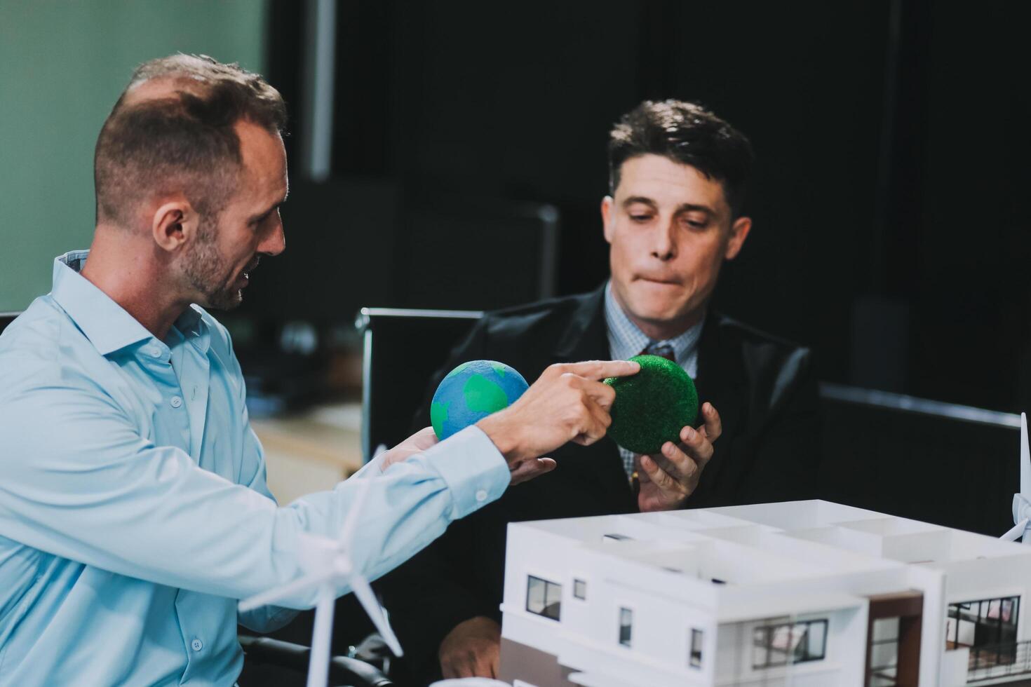 Engineers meeting about wind turbine model and house model. Renewable energy and housing development concept. Team of architects and engineers in modern office discussing design structure. photo