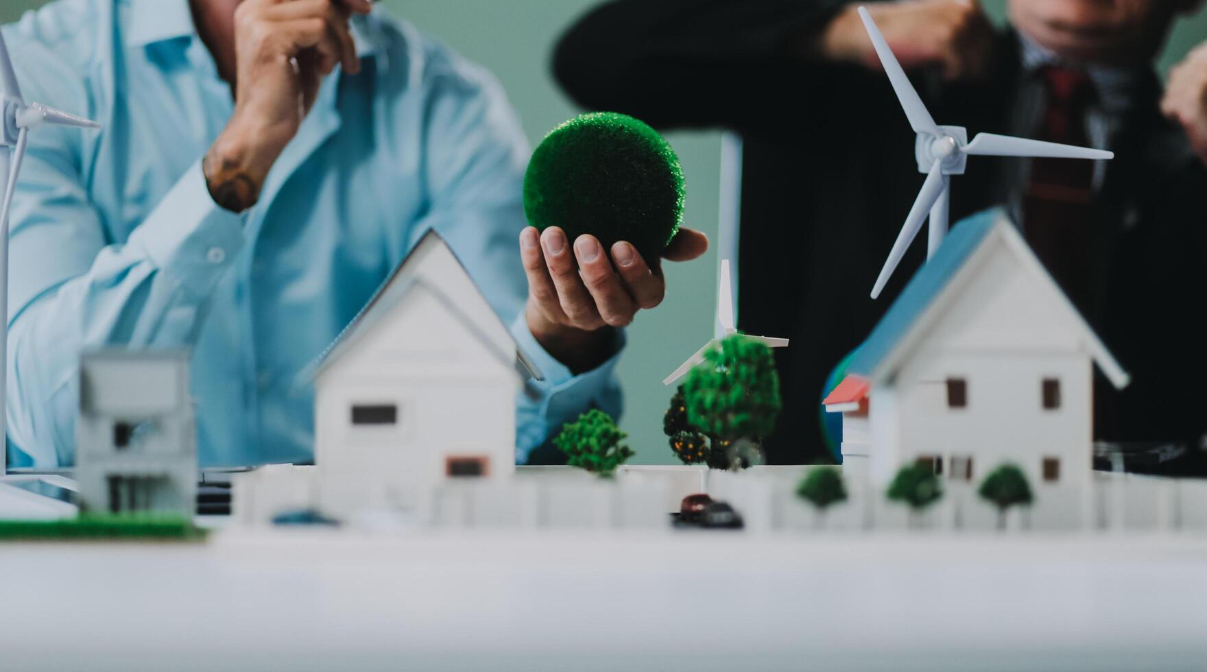 Engineers meeting about wind turbine model and house model. Renewable energy and housing development concept. Team of architects and engineers in modern office discussing design structure. photo
