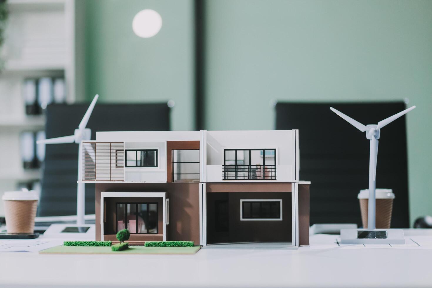 Engineers meeting about wind turbine model and house model. Renewable energy and housing development concept. Team of architects and engineers in modern office discussing design structure. photo