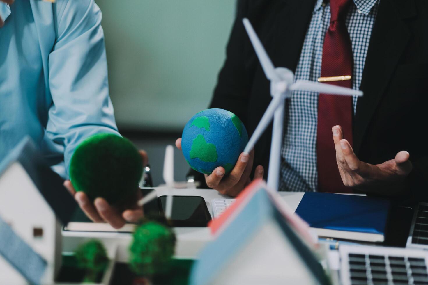 Engineers meeting about wind turbine model and house model. Renewable energy and housing development concept. Team of architects and engineers in modern office discussing design structure. photo