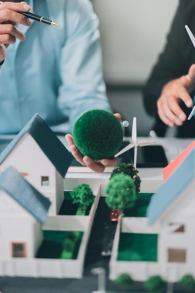 Engineers meeting about wind turbine model and house model. Renewable energy and housing development concept. Team of architects and engineers in modern office discussing design structure. photo