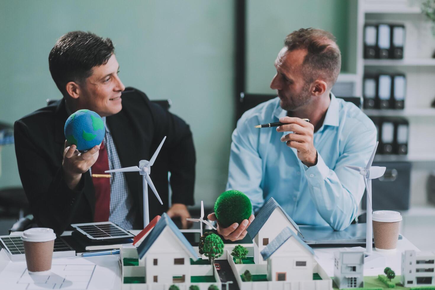Engineers meeting about wind turbine model and house model. Renewable energy and housing development concept. Team of architects and engineers in modern office discussing design structure. photo