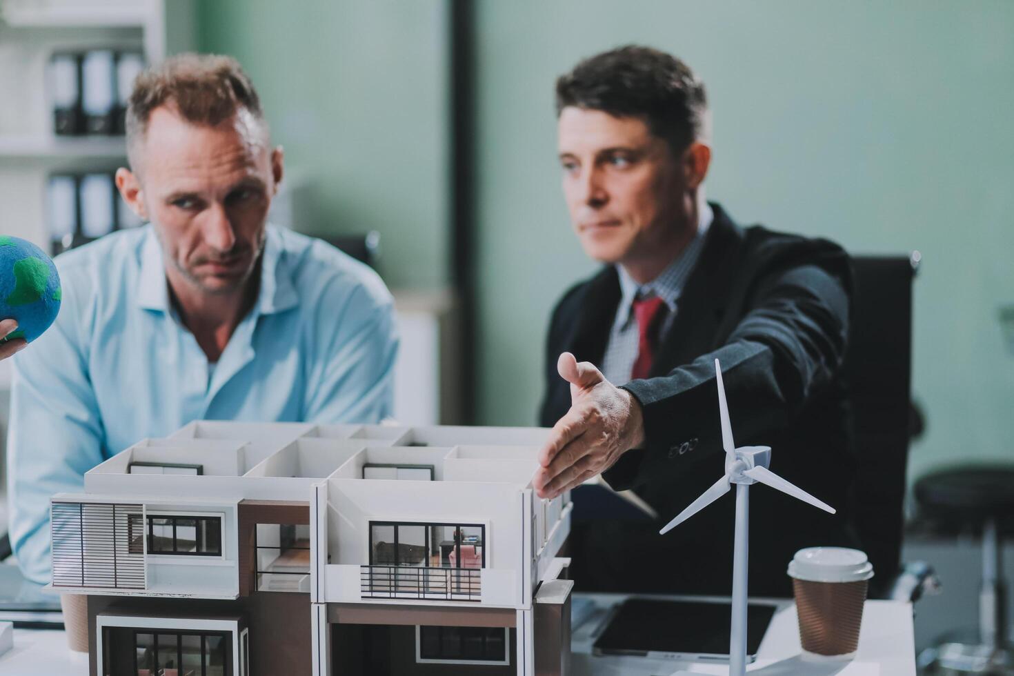 Engineers meeting about wind turbine model and house model. Renewable energy and housing development concept. Team of architects and engineers in modern office discussing design structure. photo