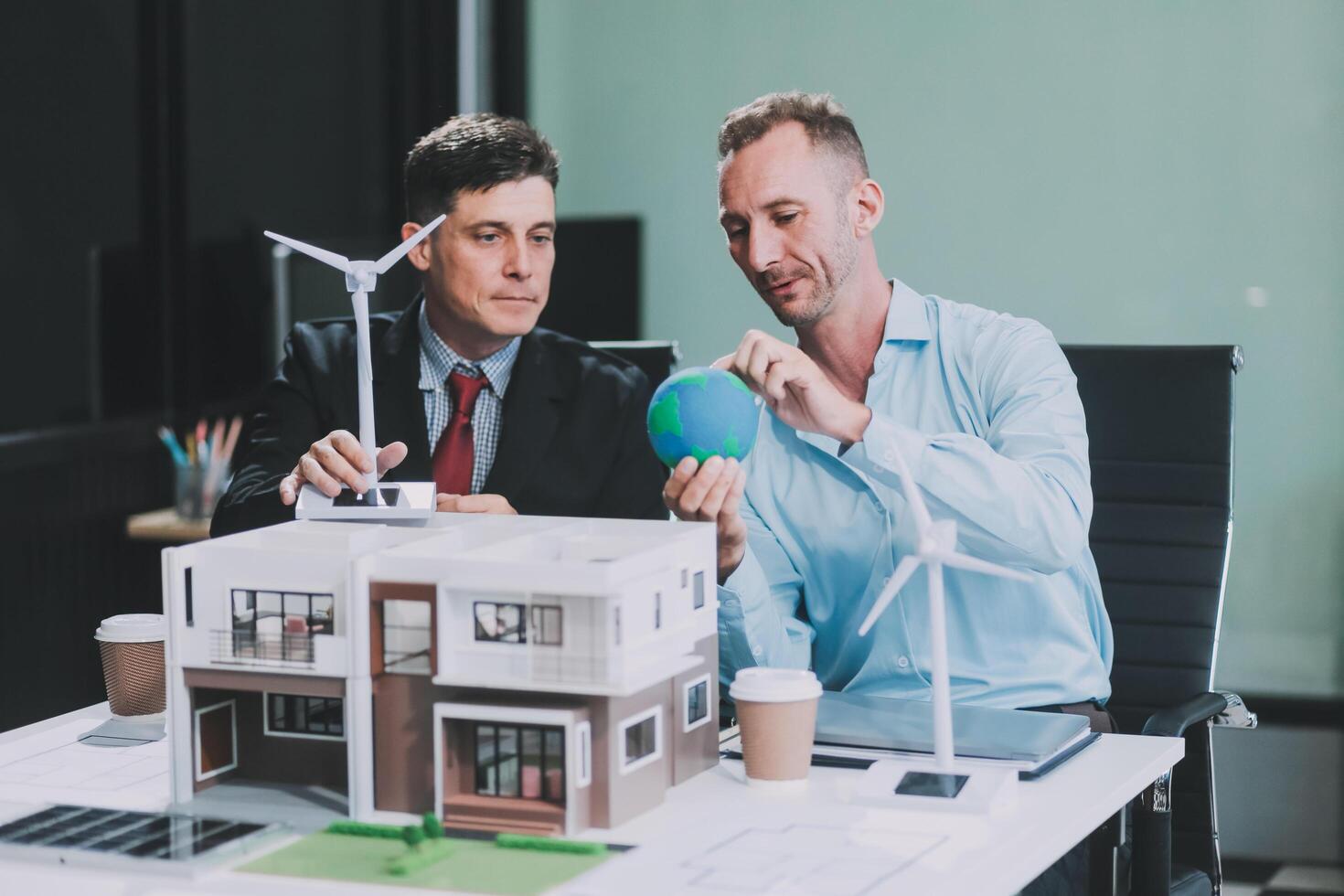Engineers meeting about wind turbine model and house model. Renewable energy and housing development concept. Team of architects and engineers in modern office discussing design structure. photo