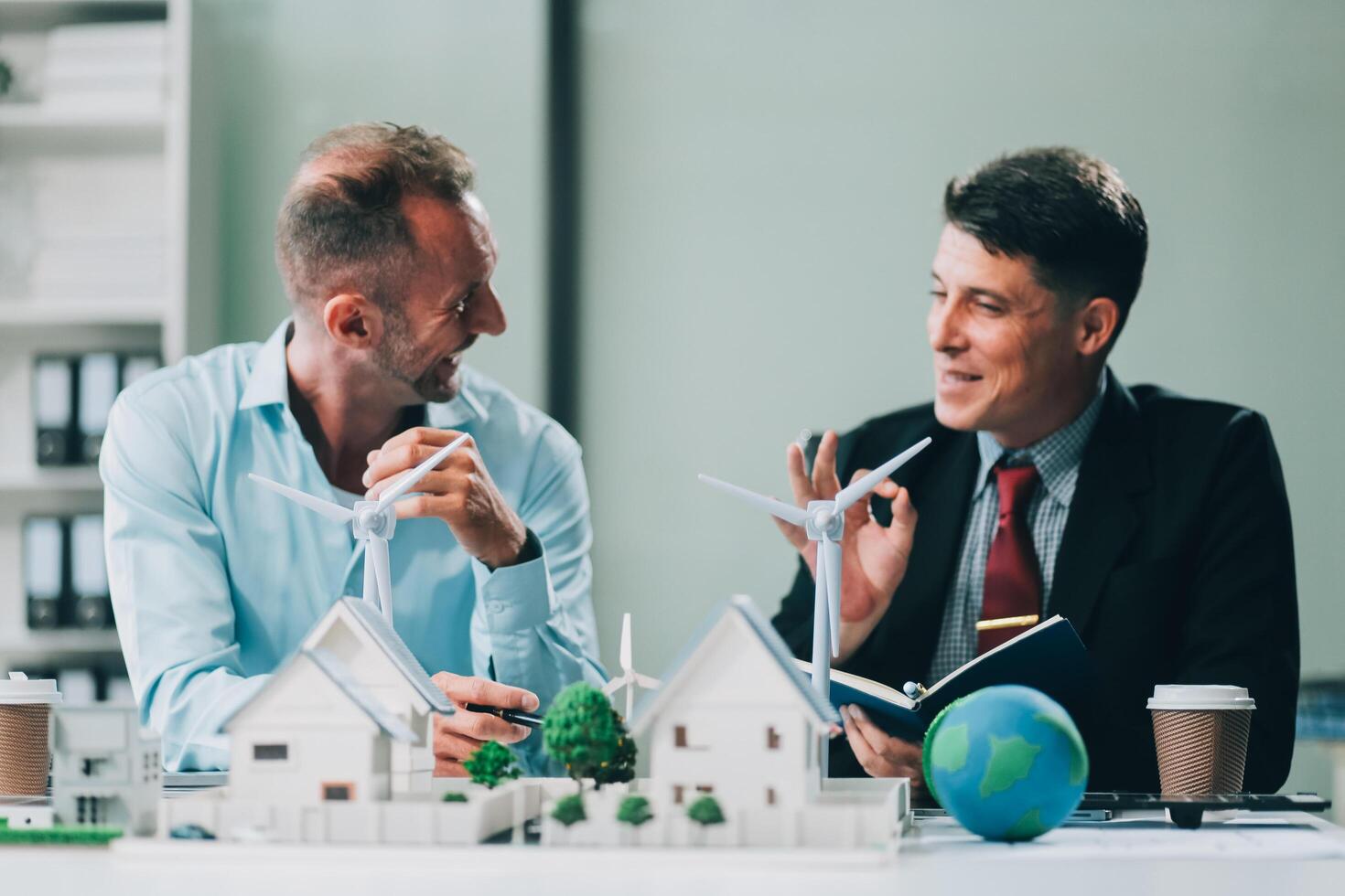 Engineers meeting about wind turbine model and house model. Renewable energy and housing development concept. Team of architects and engineers in modern office discussing design structure. photo