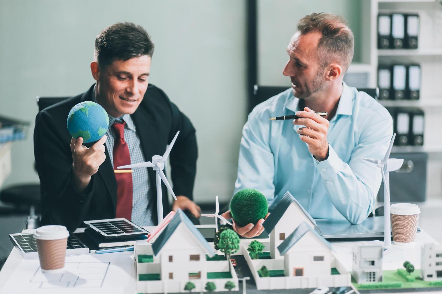 Engineers meeting about wind turbine model and house model. Renewable energy and housing development concept. Team of architects and engineers in modern office discussing design structure. photo