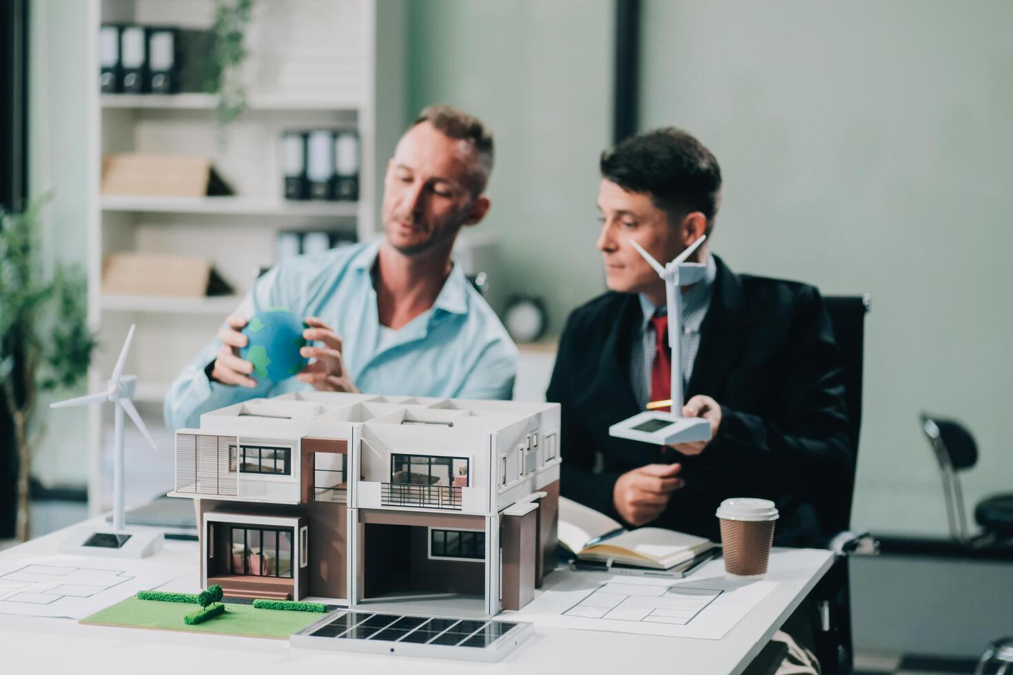 Engineers meeting about wind turbine model and house model. Renewable energy and housing development concept. Team of architects and engineers in modern office discussing design structure. photo
