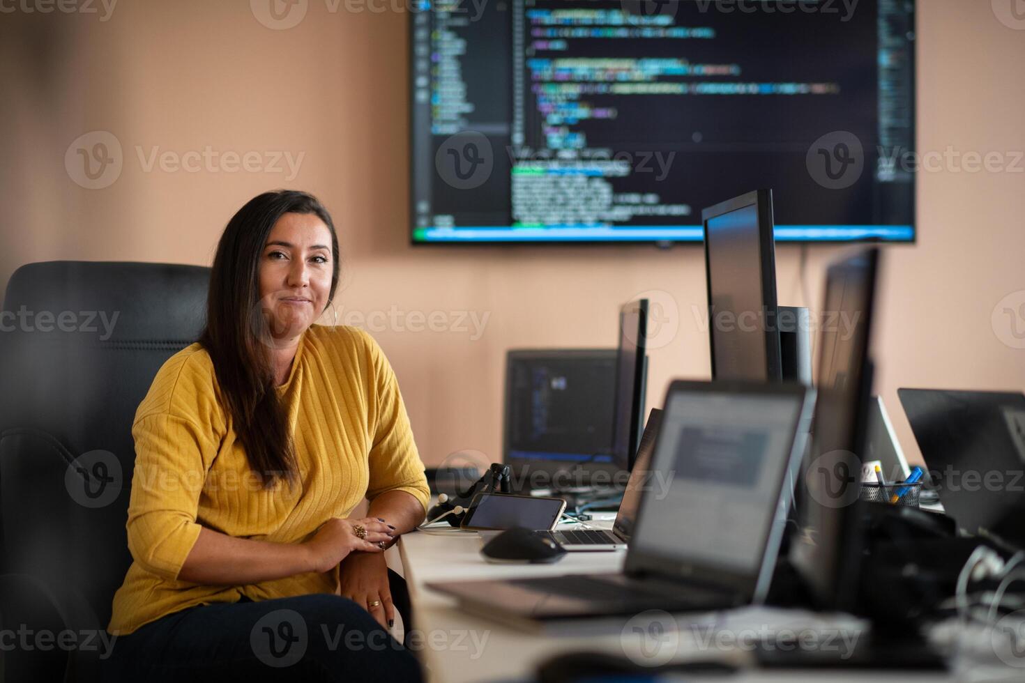 A businesswoman sitting in a programmer's office surrounded by computers, showing her expertise and dedication to technology. photo