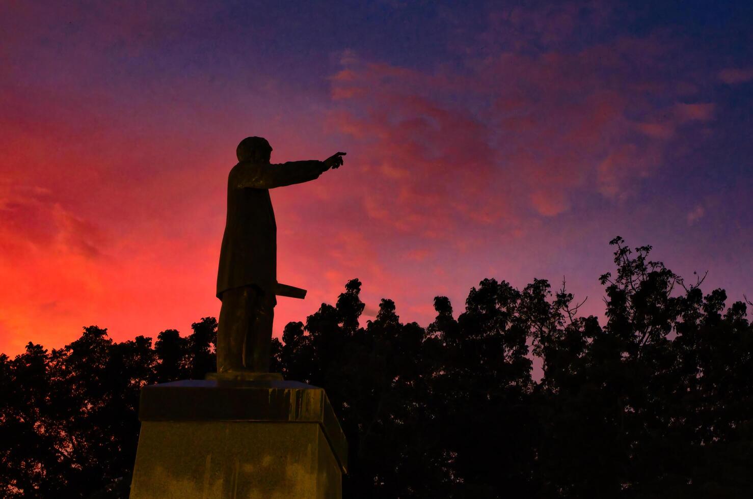 A statue of a man holding a gun in front of a colorful sunset photo