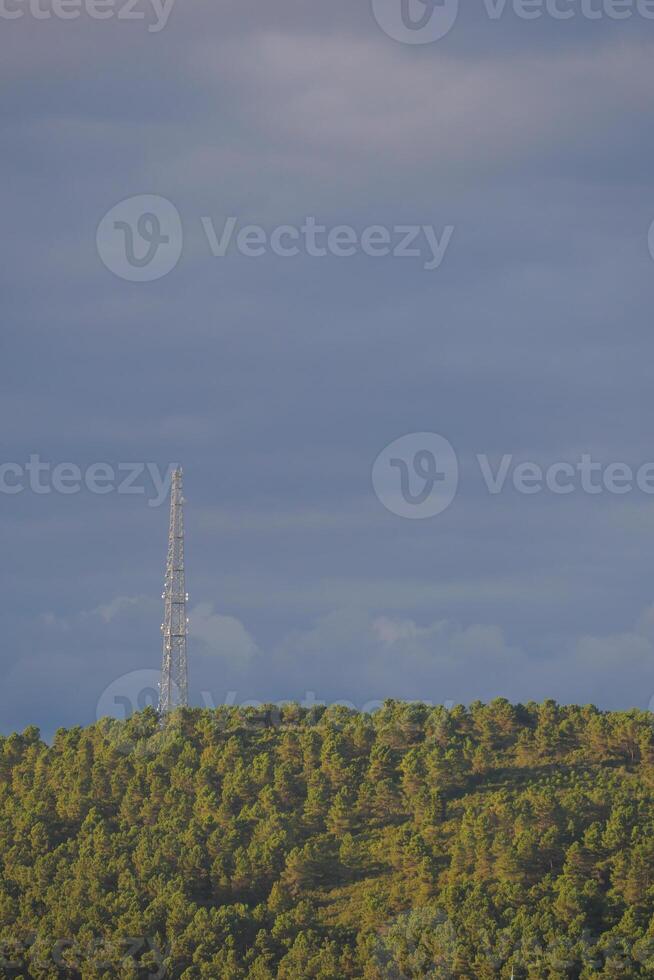 A Telecommunication Tower Standing Tall on a Lush Green Hill Beneath a Dramatic Sky Full of Clouds photo