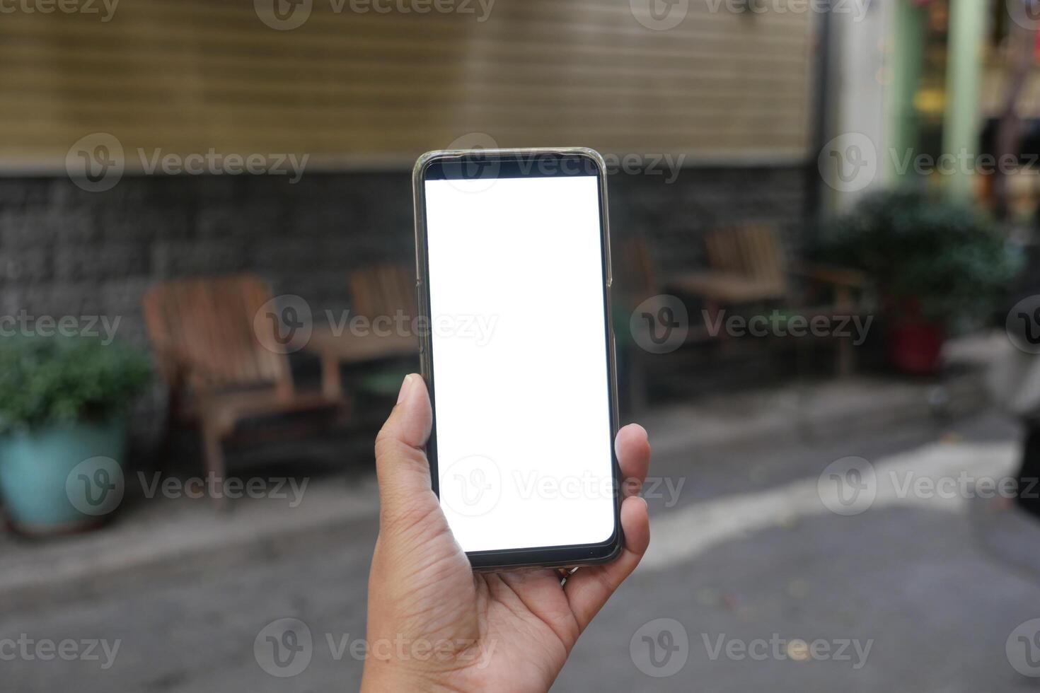 A hand is holding a smartphone with a blank screen while in a beautiful outdoor setting photo