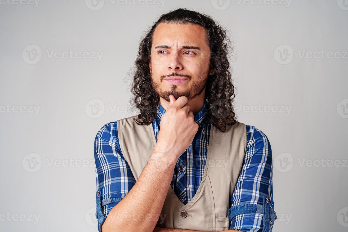 A man with curly hair thoughtfully pondering in a neutral background photo