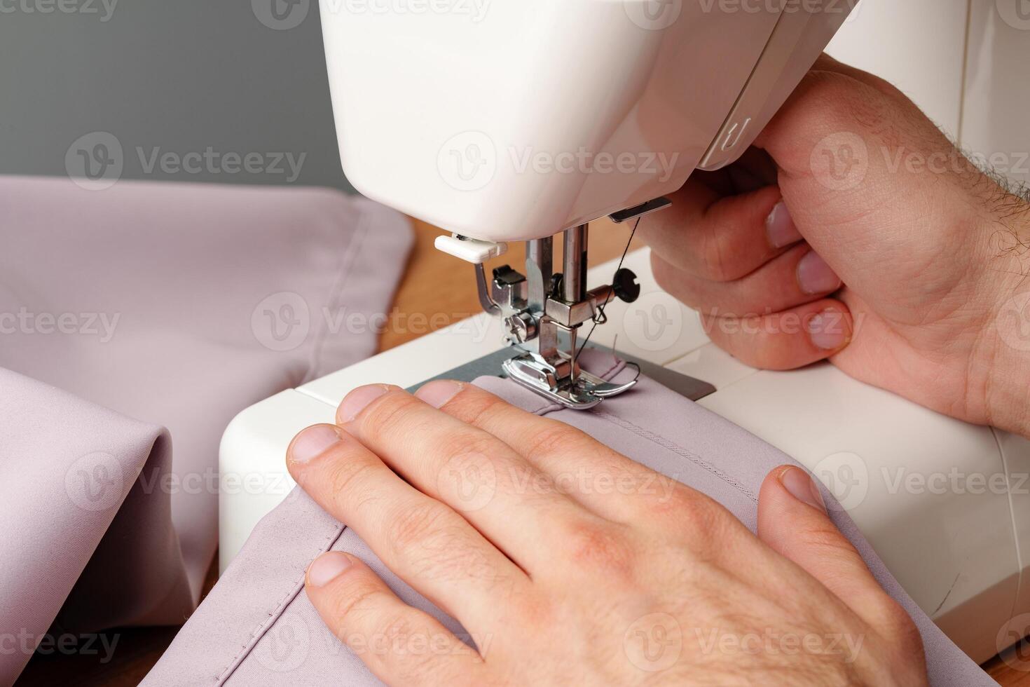 Hands sewing fabric using a sewing machine on a wooden table in a well-lit workspace photo