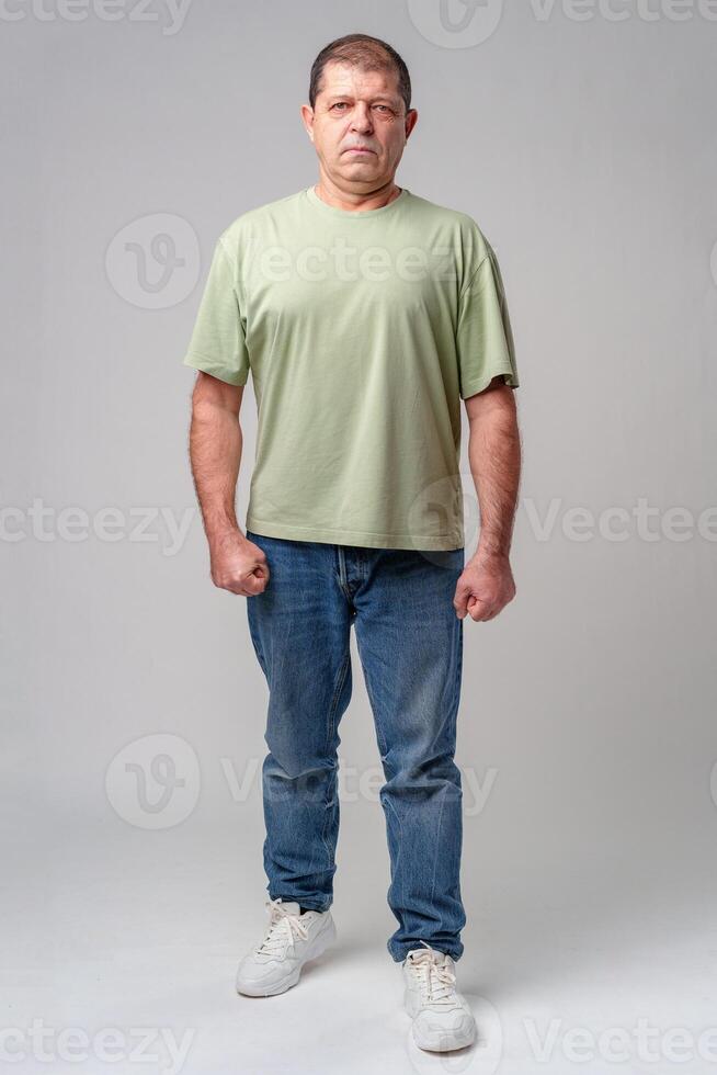 Man in casual attire standing posed against a neutral background, displaying a serious expression photo