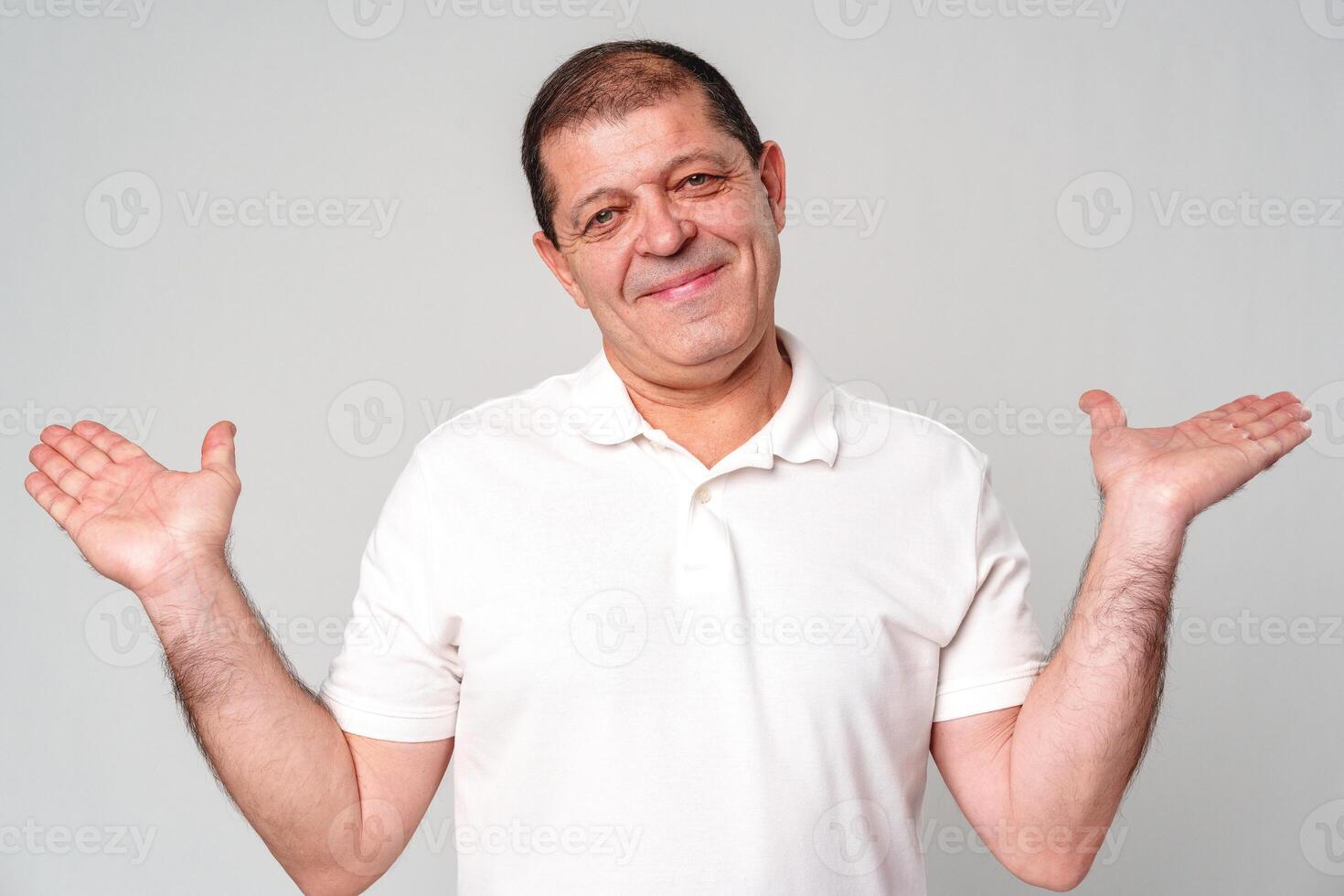 Smiling man in a white shirt gestures with open palms against a light gray background photo