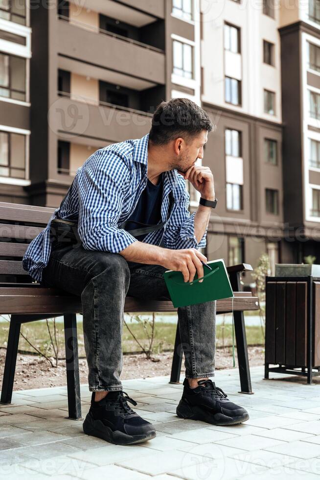 A person writes in a notebook while sitting on a park bench photo