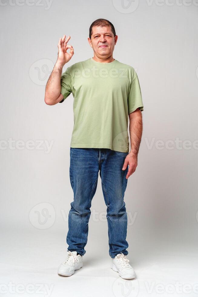 A man with a slight smile making an OK hand gesture against a neutral background photo