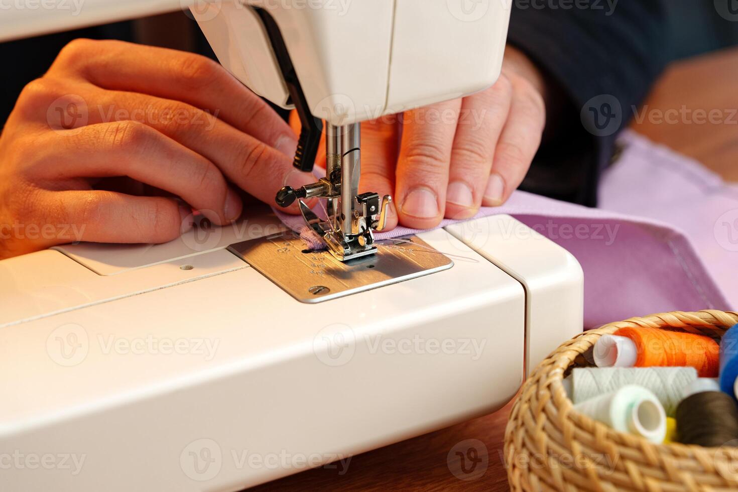 Hands sewing fabric using a sewing machine on a wooden table in a well-lit workspace photo