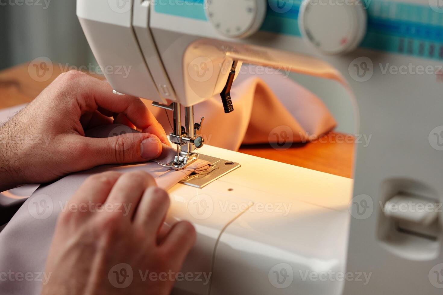 Hands sewing fabric using a sewing machine on a wooden table in a well-lit workspace photo