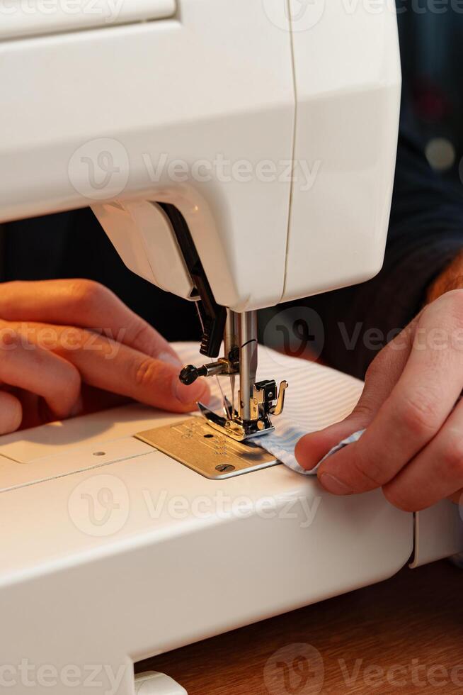 Hands sewing fabric using a sewing machine on a wooden table in a well-lit workspace photo