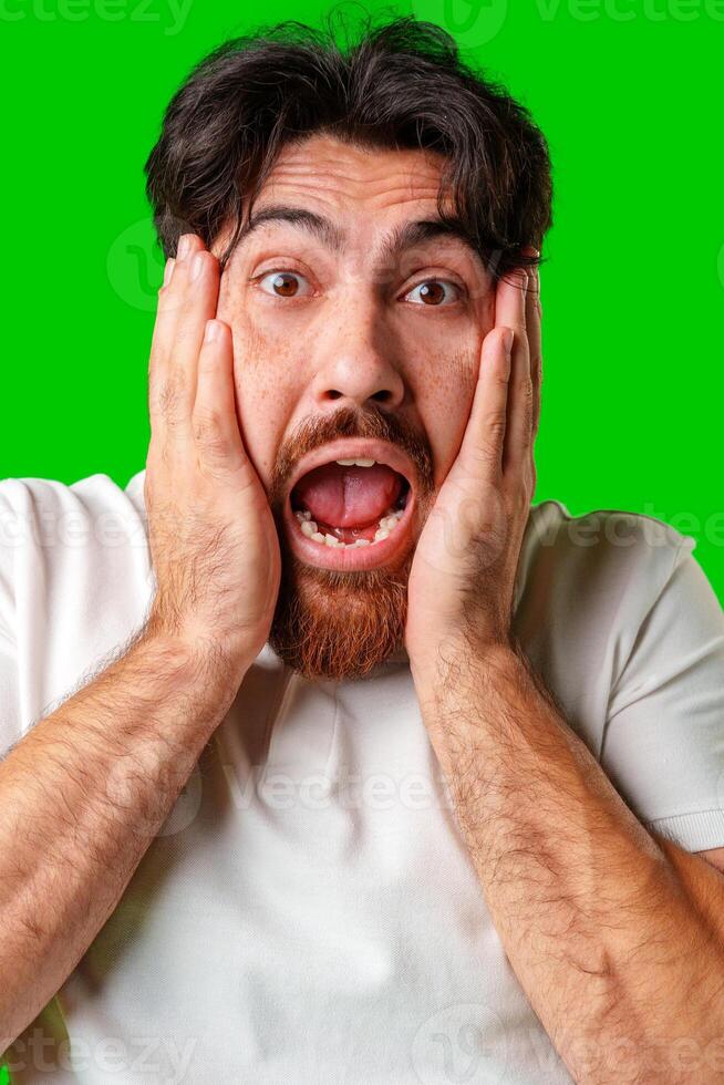 A man with a surprised expression holds his face while against a vibrant green background photo