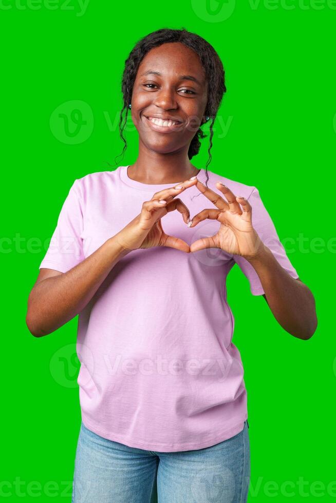 A young woman expresses love by forming a heart shape with her hands against a bright green background photo