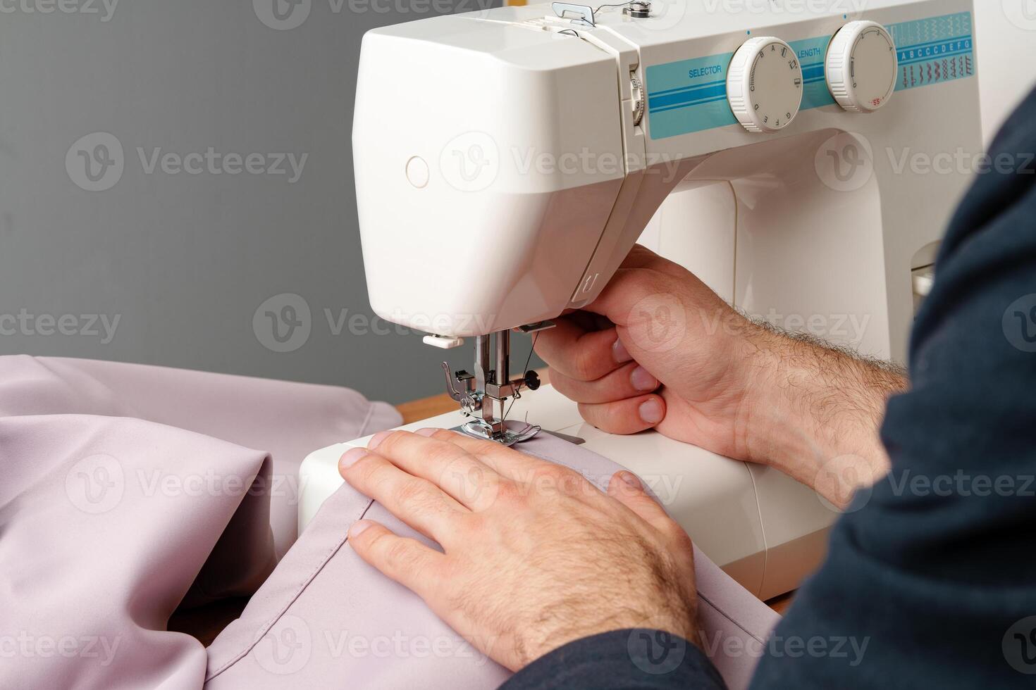 Hands sewing fabric using a sewing machine on a wooden table in a well-lit workspace photo