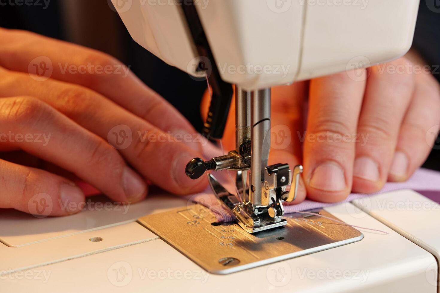 Hands sewing fabric using a sewing machine on a wooden table in a well-lit workspace photo