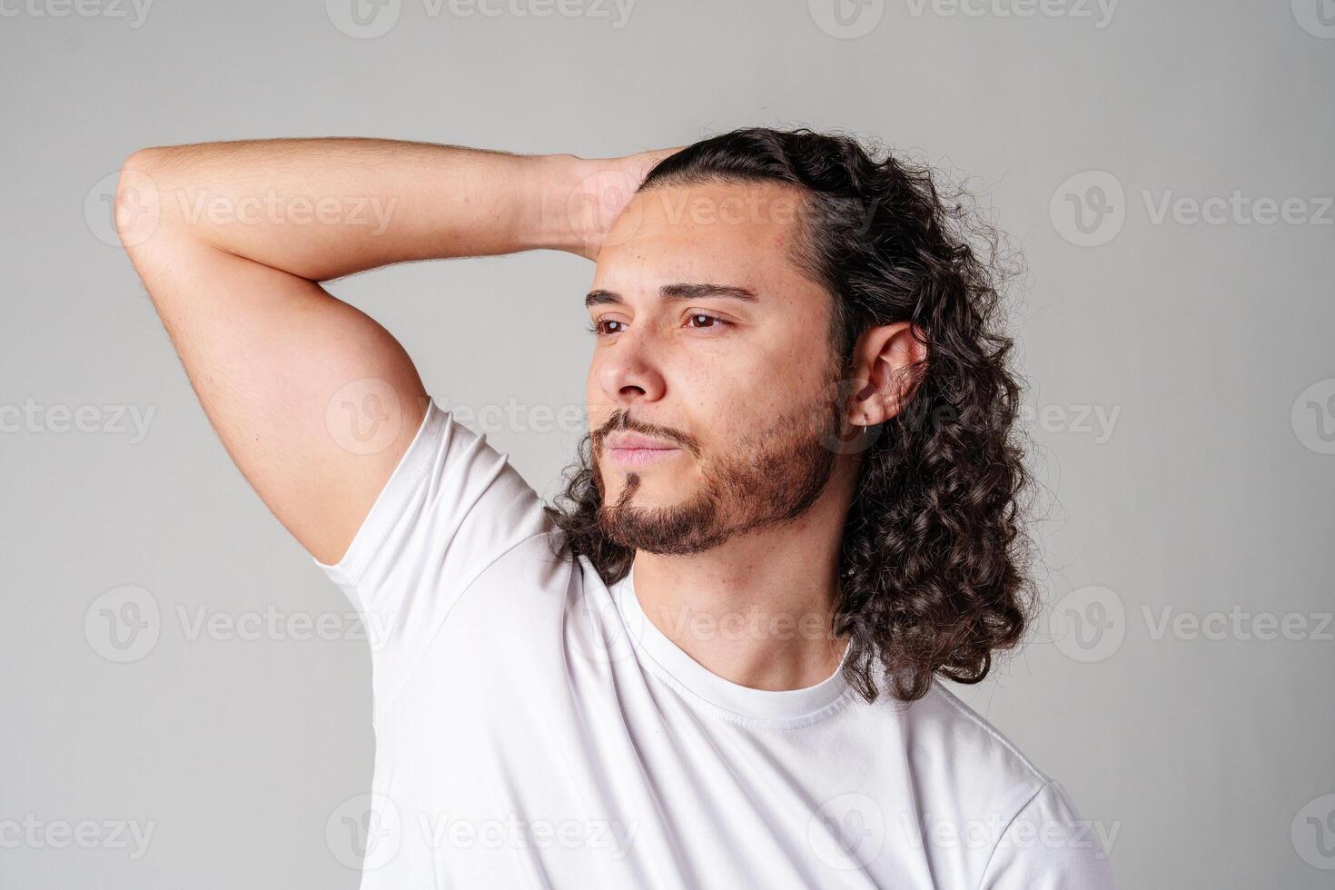 Young man with curly hair poses confidently against a plain background photo